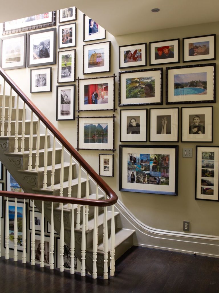 a group of family photos arranged on a wall around a staircase with a wrap around banister