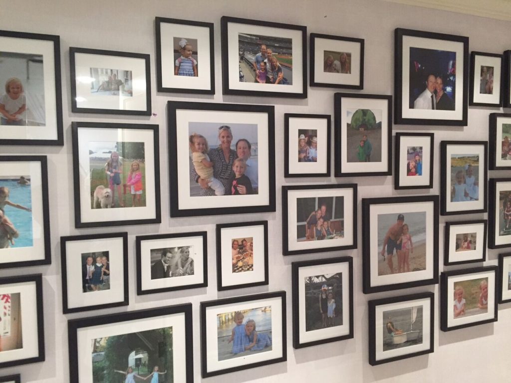 A variety of sizes of rectangular and square black frames with family photos arranged on a wall.