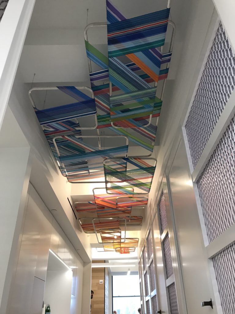 An installation of objects made of lawn chair webbing installed on a ceiling