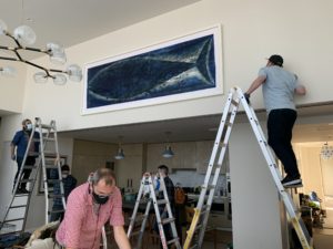 art installers work together to install a whale painting