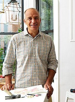 Photo of white man in his sixties, holding paper and standing next to hammer