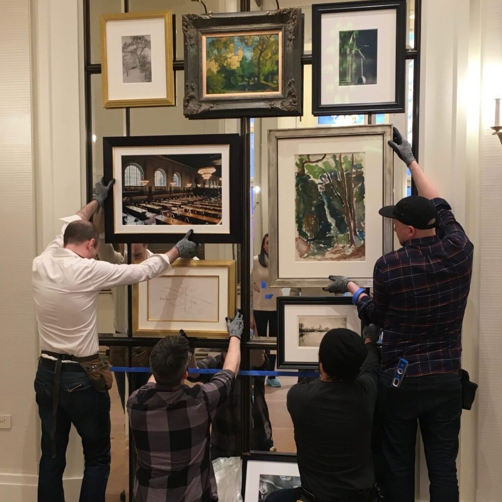 four art handlers carefully placing multiple frames on a mirror wall
