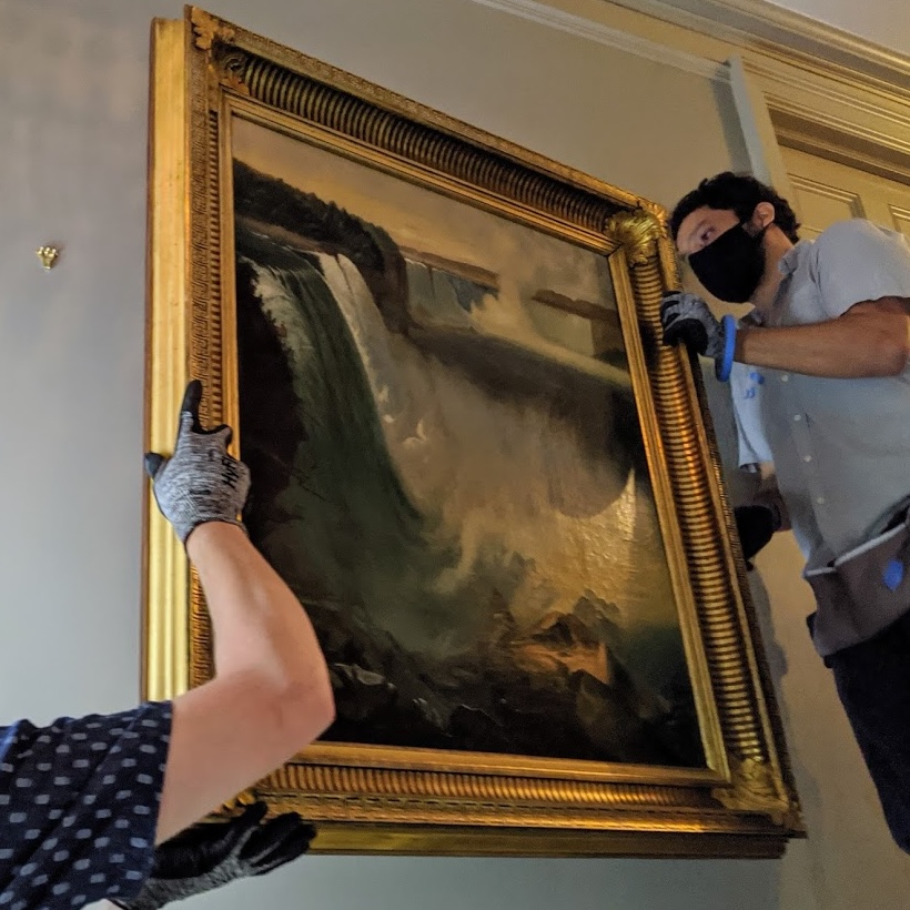 Two art handlers moving large golden frame onto wall