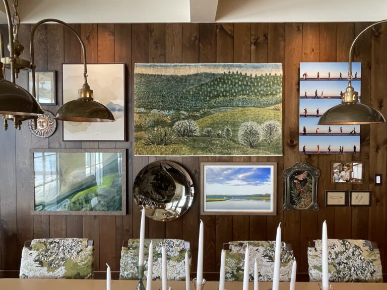 Gallery wall installation in a dining room with wood-paneled walls, featuring paintings, photography, a tapestry, and a mirror arranged by ILevel