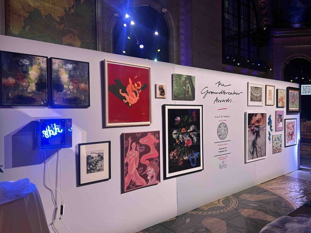 Section of the Housing Works Groundbreaker Awards silent auction wall featuring neon art and paintings, with ILevel credit visible