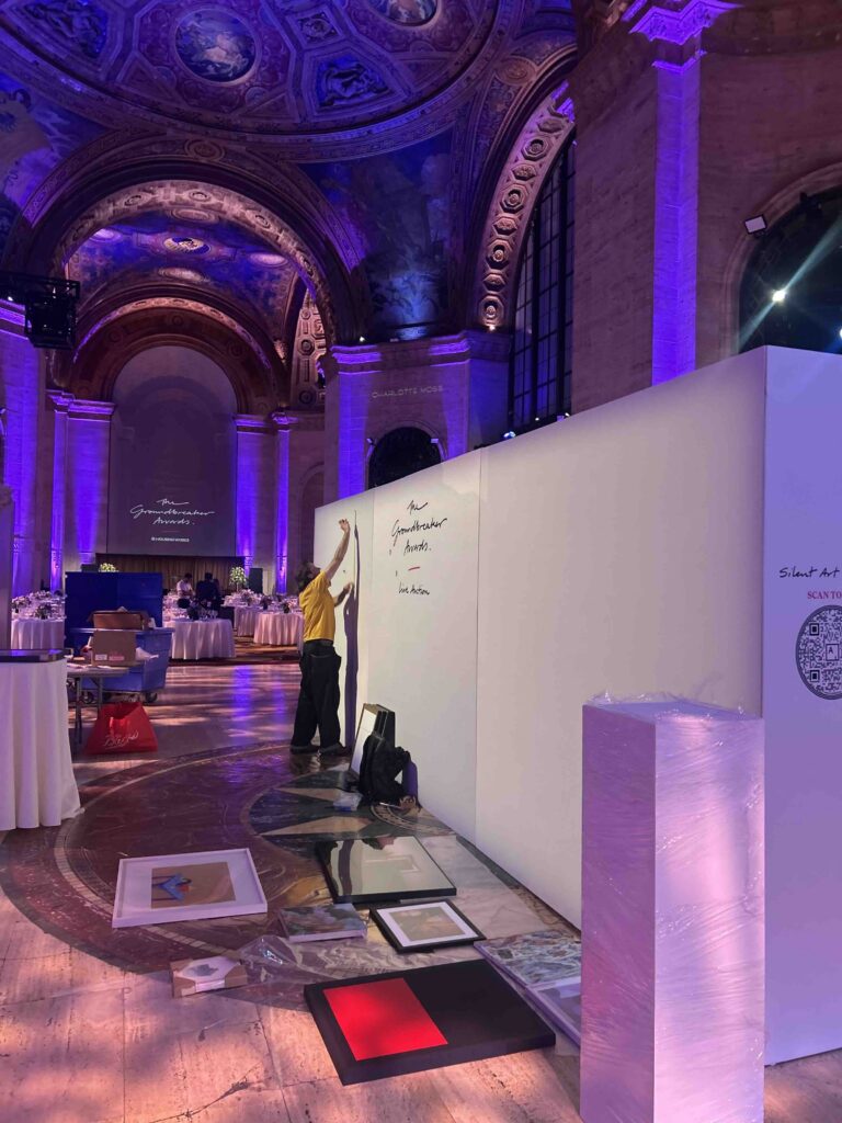 ILevel art handler taping out layout on an empty wall before installation at the Housing Works Groundbreaker Awards Gala