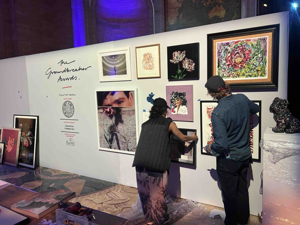 Two ILevel art handlers installing artwork on the wall during setup for the Housing Works Groundbreaker Awards silent auction