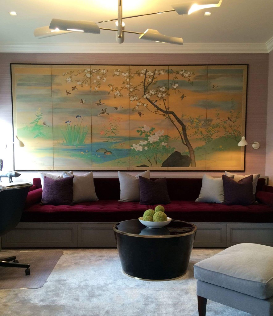A large multi-panel Japanese folding screen depicting birds, blossoming cherry trees, and a stream in gold and pastel tones, mounted flush on a wall above a built-in burgundy velvet bench in a luxury residential room.