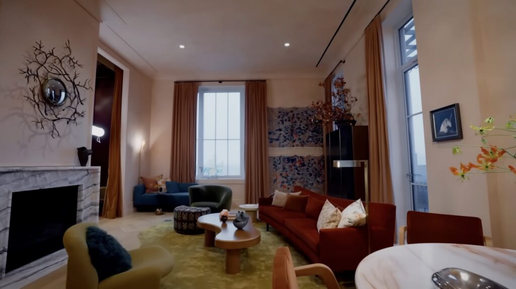 Wide view of the living room in Kate Upton Justin Verlander NYC penthouse showing tapestry wall hanging and sculptural branch mirror above fireplace, designed by John Ruggiero