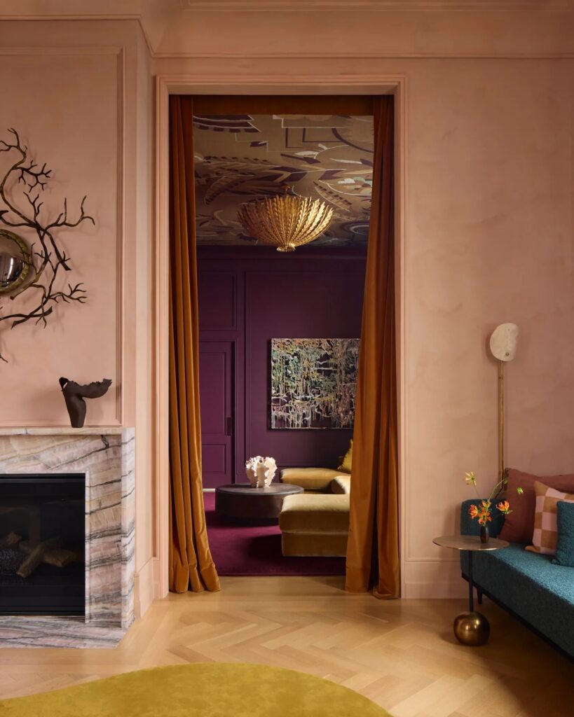 Gold velvet curtains framing the passage between living room and screening room in John Ruggiero-designed NYC penthouse, with sculptural branch mirror visible beside fireplace