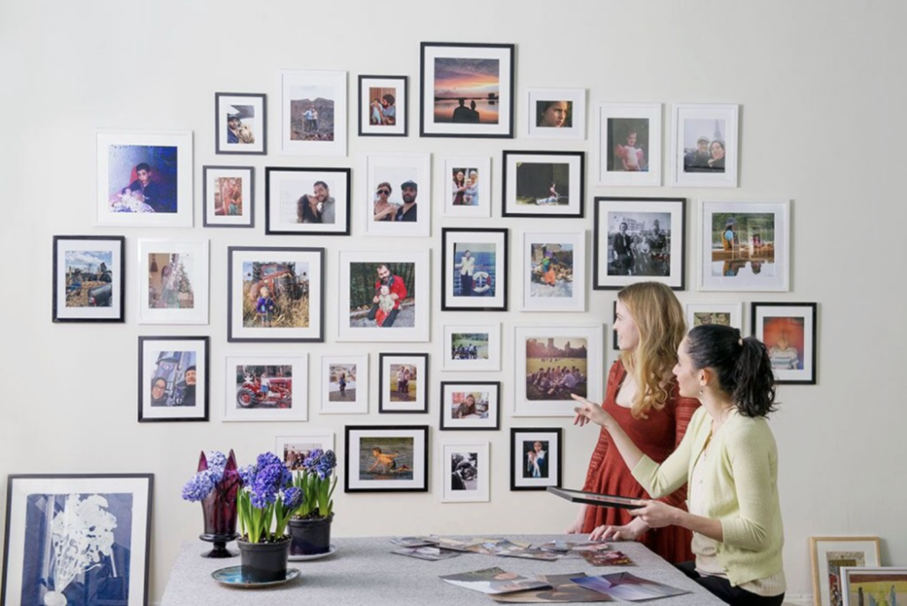 Two women working and pointing to a gallery wall of framed photos