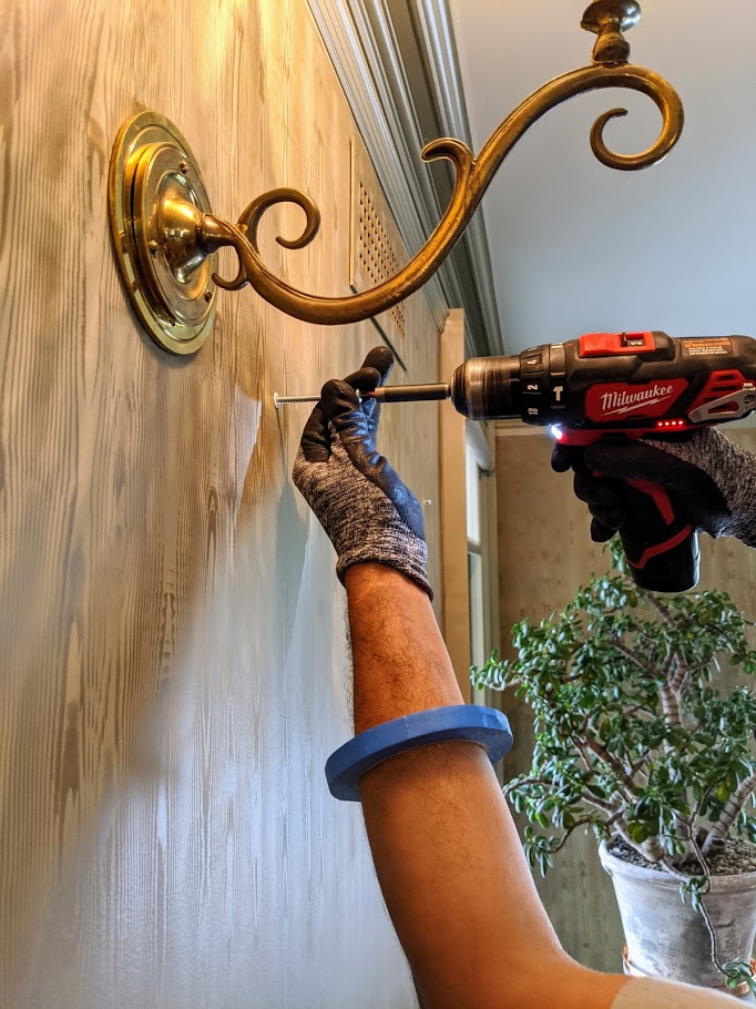 ILevel art installer using a drill to mount hardware on a wood-paneled wall