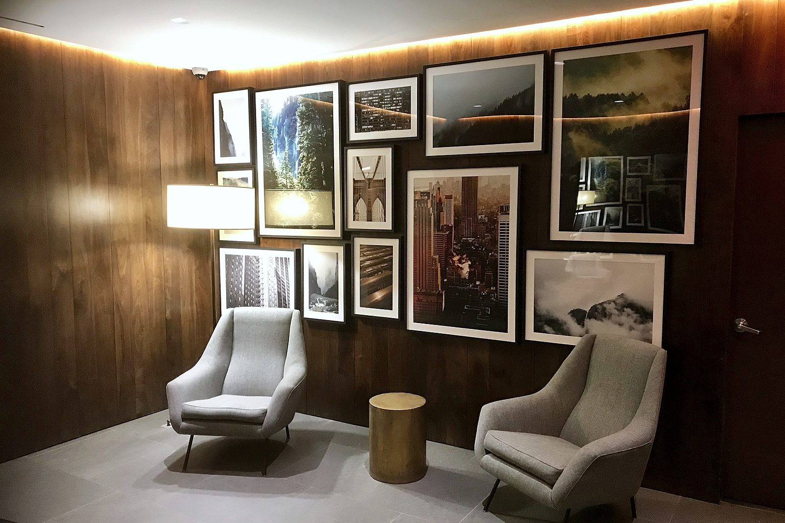 Salon-style arrangement of framed photographs on a walnut wall above two lounge chairs
