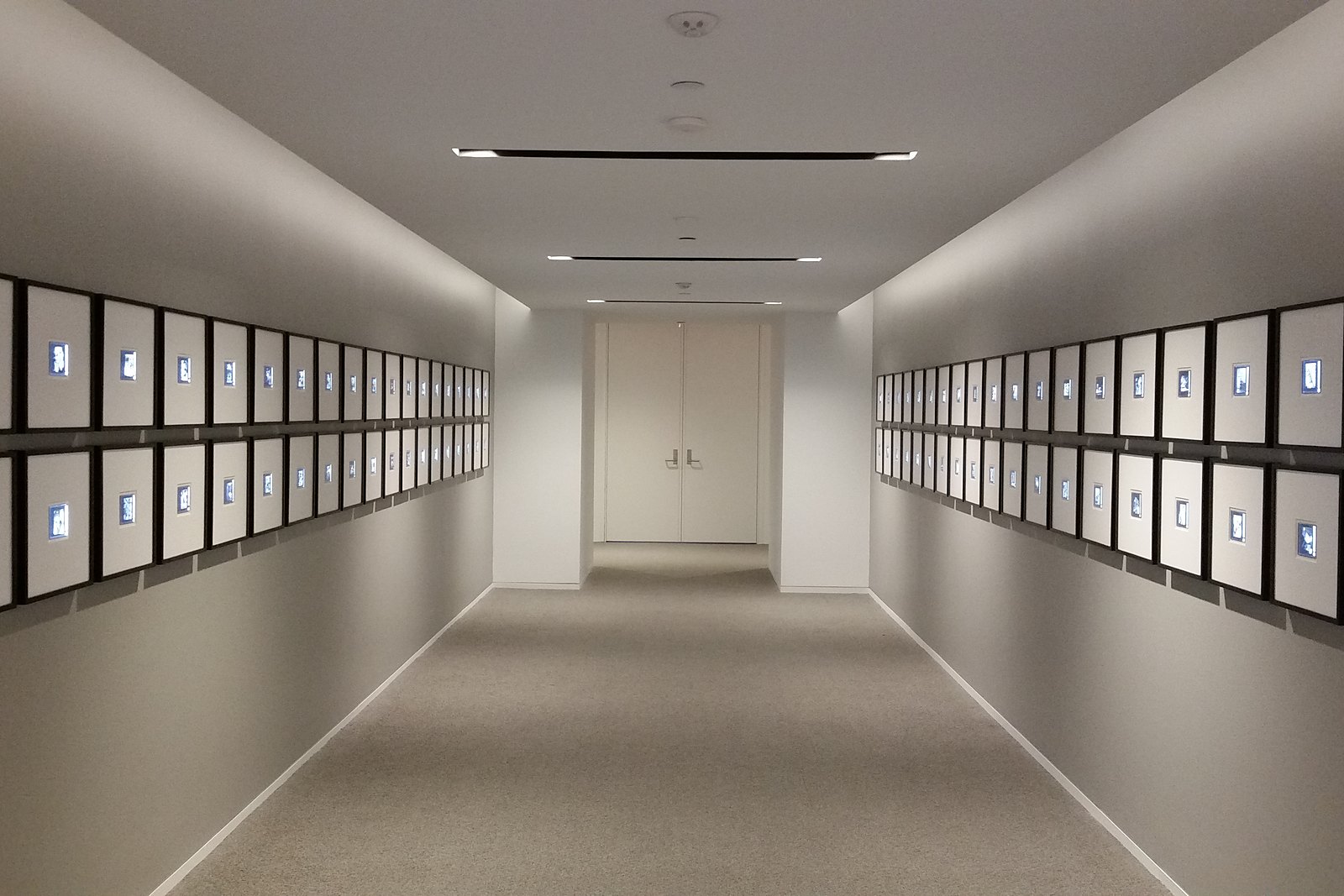 Long corridor lined on both walls with two rows of evenly lit framed photographs