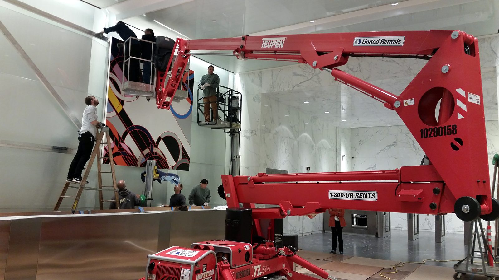 ILevel crew using a lift to install a large geometric painting in a marble office lobby