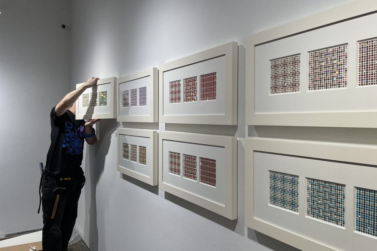 Installer aligning framed artwork within a precision grid on an office wall.