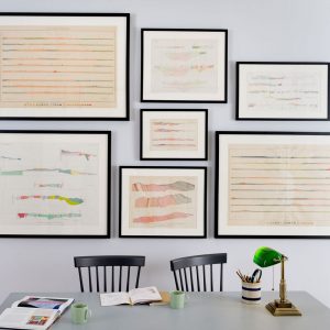 7 black frames hang on grey wall above green table and black chairs, artwork is fine art parchment