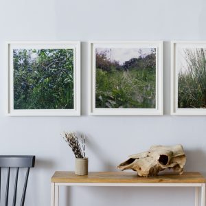three white frames hung on grey wall above small table and black chair