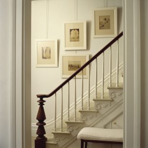photo of white wall with 4 pictures hanging behind a stair rail